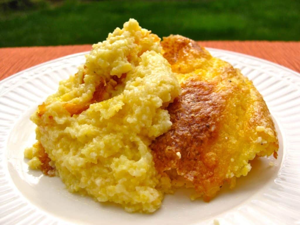 A serving of warm and wonderful Cheese Grits Casserole scooped onto a white serving plate.