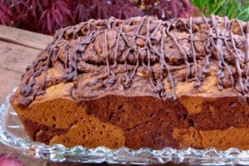 A loaf of marbled Pumpkin Chocolate Bread drizzled with chocolate on a glass plate in an autumn garden.