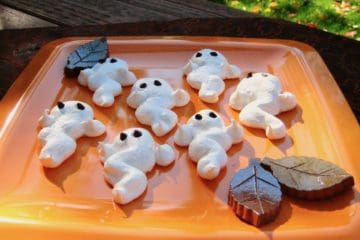 Meringue Ghost Cookies on an orange plate with ceramic leaf decorations.