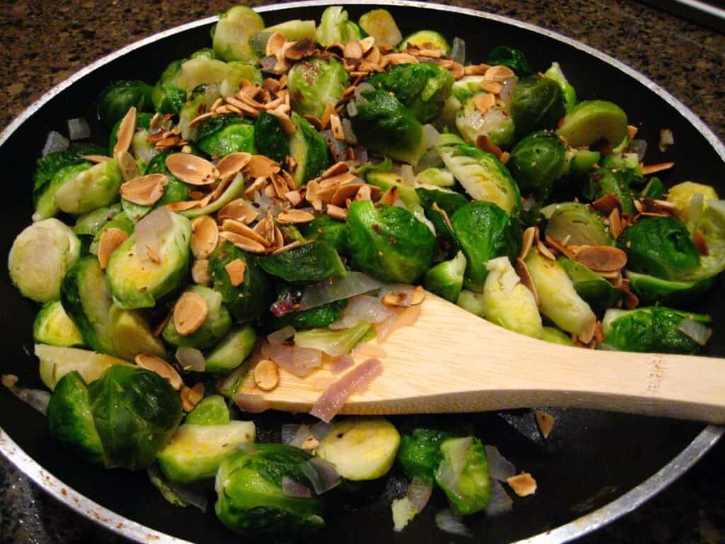 Brussels Sprouts with Almonds in a skillet with wooden spatula.