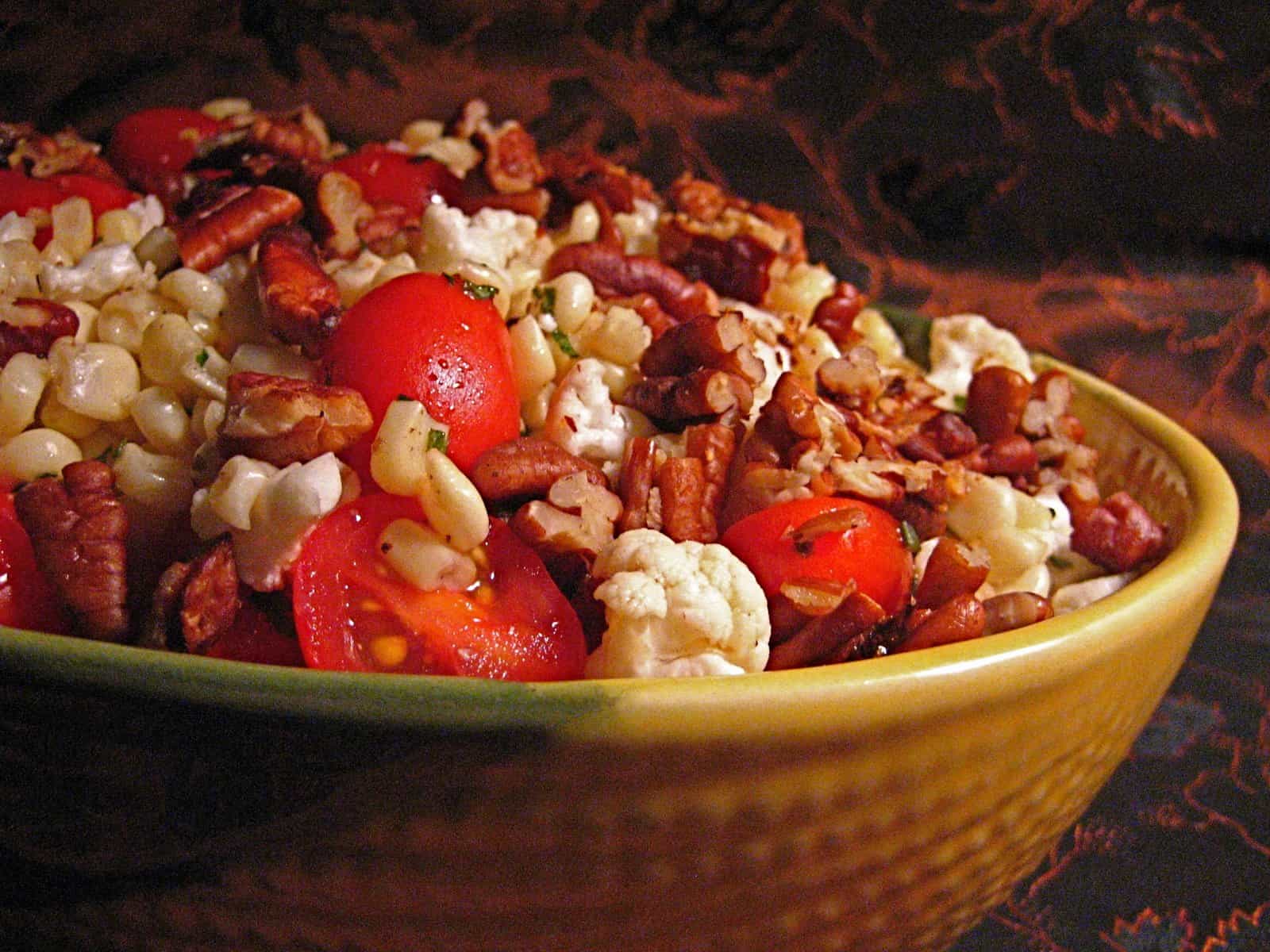 Corn Salad with Pecan Dressing topped with pecan pieces in a decorative corn bowl
