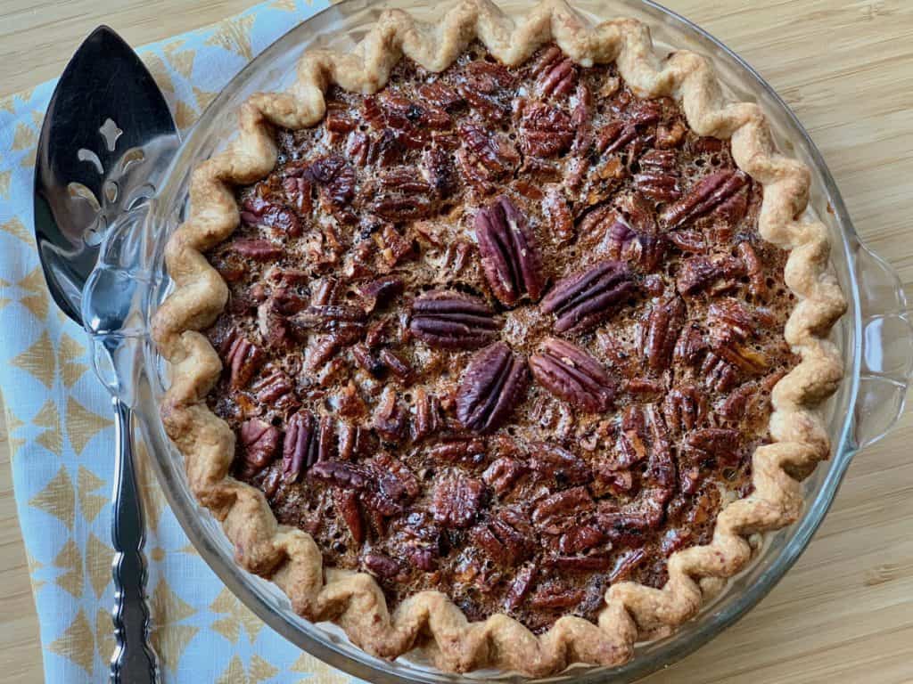 A Beautiful Pecan Pie topped with a starburst of pecans beside a pie server and folded napkin.