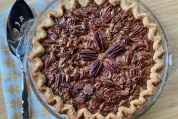 A Beautiful Pecan Pie topped with a starburst of pecans beside a pie server and folded napkin.