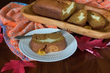 A sliced loaf of Pumpkin Ribbon Bread on a wooden tray beside a slice served on a white plate with a fork.