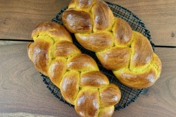 Two braided loaves of Pumpkin Yeast Bread on a black wire rack set on a wooden table.