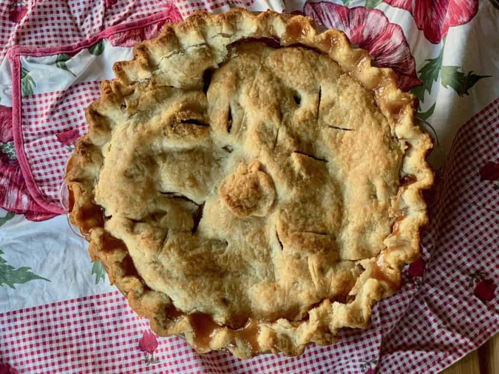 A whole Rustic Apple Pie displayed on a vintage apron, viewed from overhead