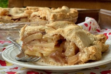 A slice of Rustic Apple Pie on a plate atop a vintage apron with the cut pie in the background.