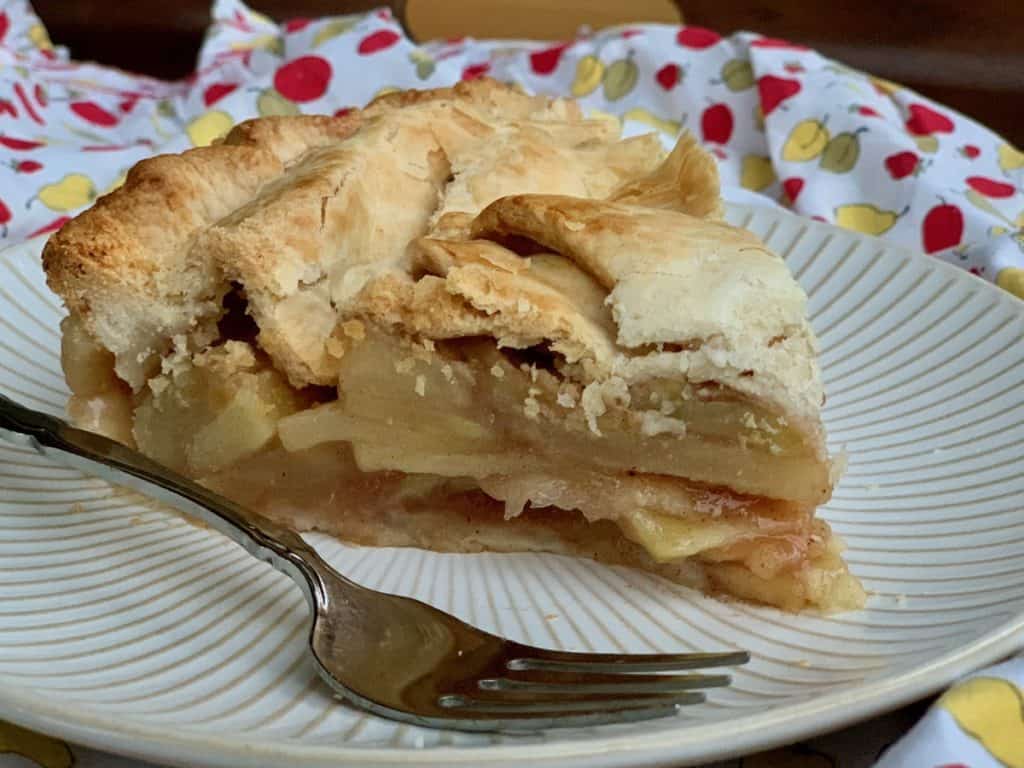 A slice of Rustic Apple Pie served on a white plate with a fork.
