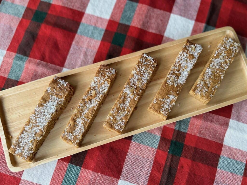 A row of Ginger Cookie Sticks on a wood tray on top of a red plaid napkin.