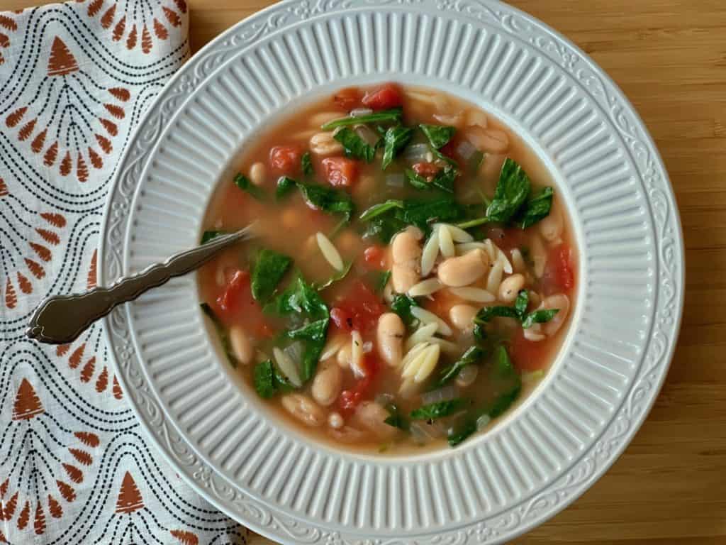 Italian Supper Soup, made with orzo, white beans, and spinach in a vegetable broth, served in a shallow white bowl. 