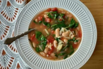 Italian Supper Soup, made with orzo, white beans, and spinach in a vegetable broth, served in a shallow white bowl.