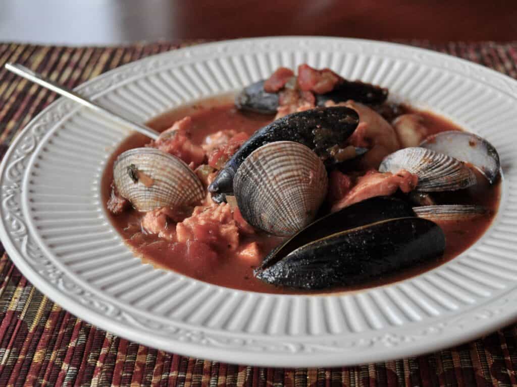 A bowl of Northwest Cioppino filled with mussels, clams, and salmon, in a low white bowl.