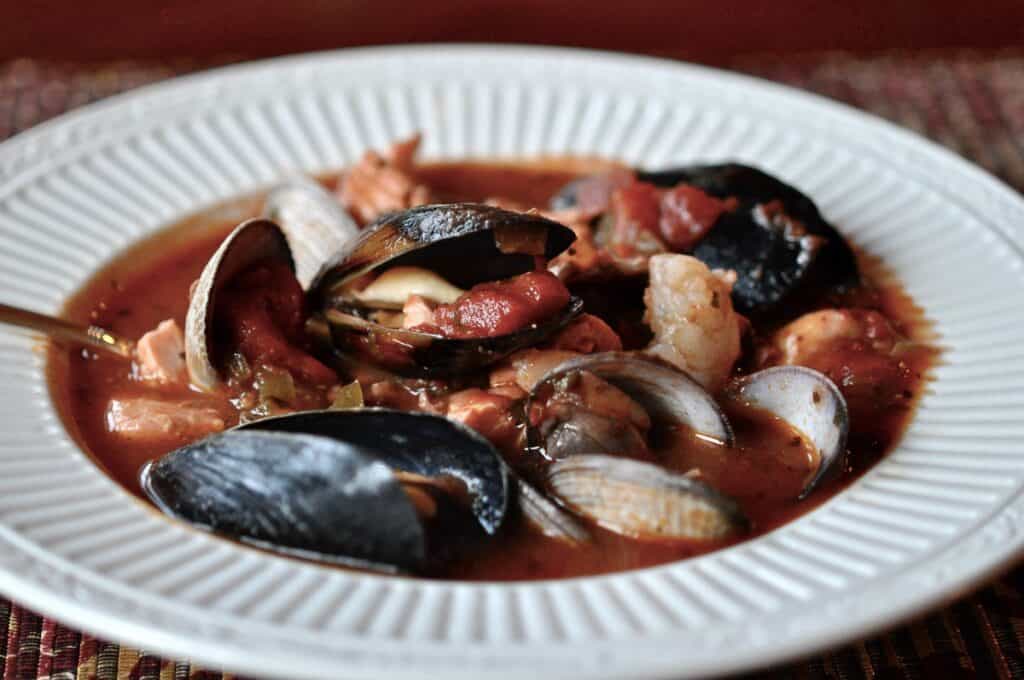 A bowl of Northwest Cioppino filled with mussels, clams, and salmon, in a low white bowl.