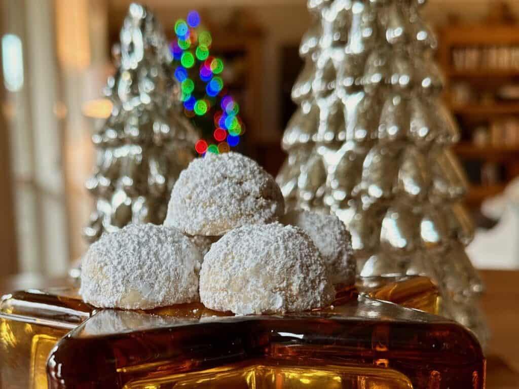 Russian Teacakes displayed with a lit Christmas Tree in the background.