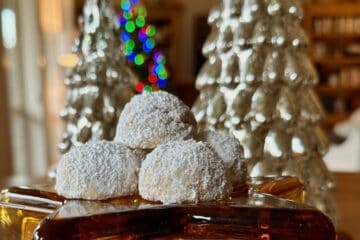 Russian Teacakes displayed with a lit Christmas Tree in the background.