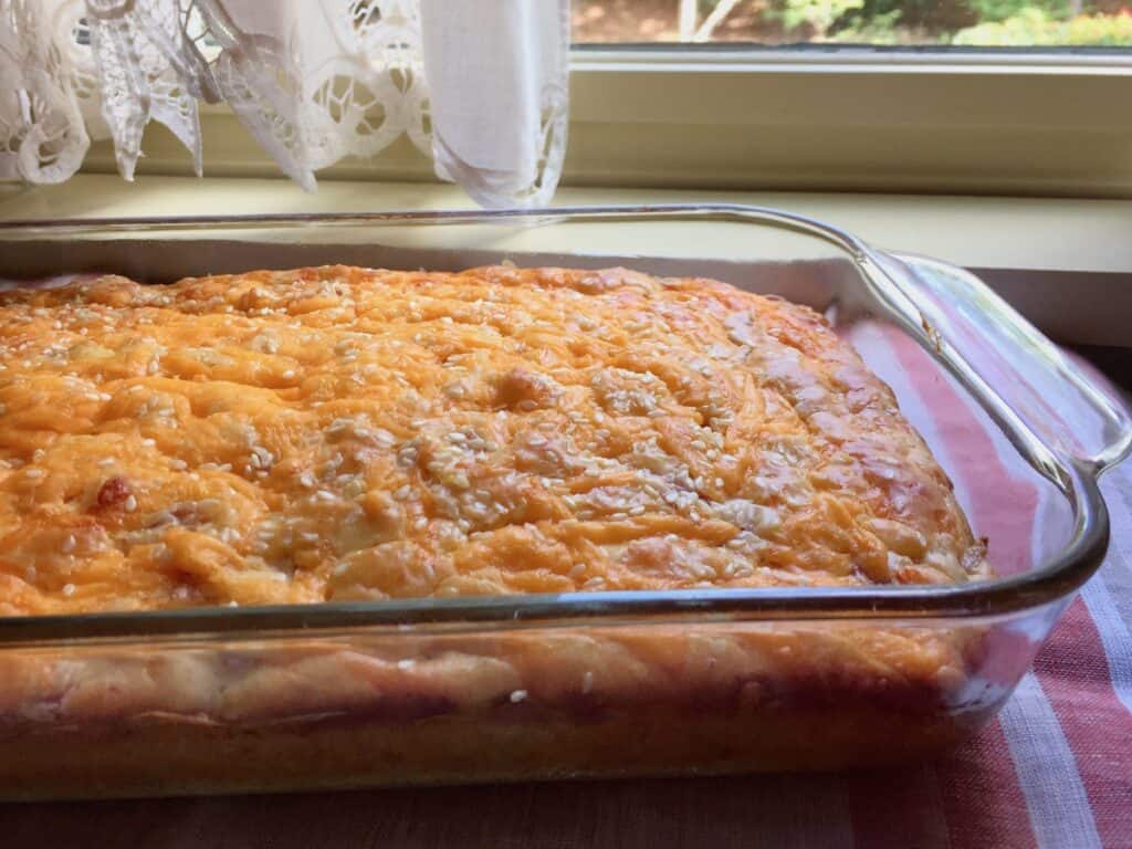Ham and Cheese Bread, baked in a 9" x 13" pyrex casserole dish, is resting in front of a kitchen window with white curtains.