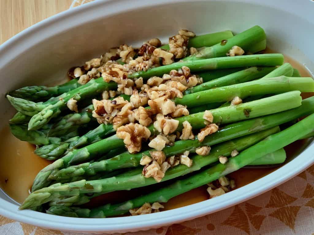 Asparagus with Walnut Dressing in a white oval serving dish.