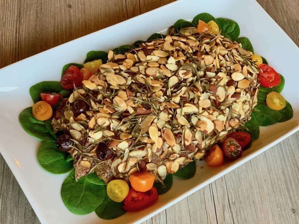 Rosemary and almond crusted Groundhog Day Meatloaf on a bed of spinach leaves with cherry tomatoes served on a rectangular platter.