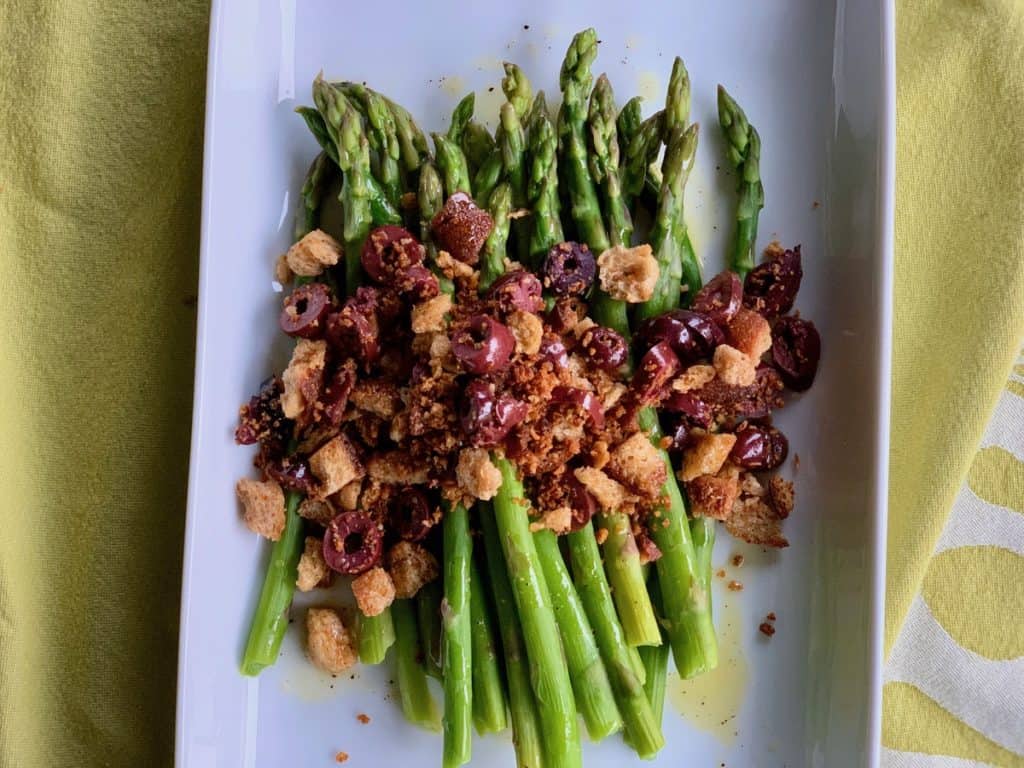 Asparagus spears with a vinaigrette dressing and a topping of toasted crumbs and olives.