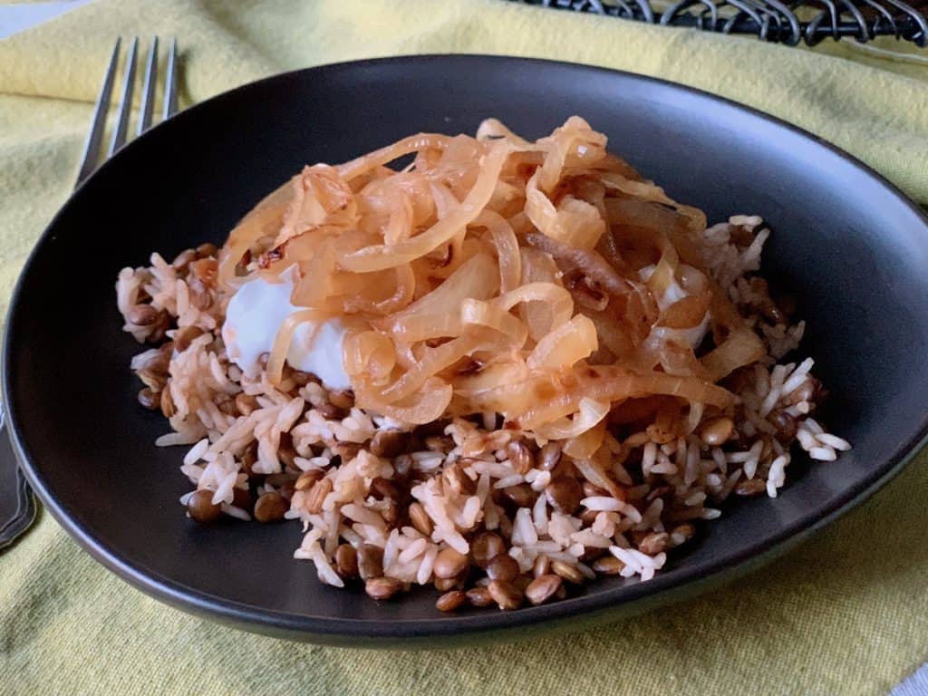 Egyptian Rice and Lentils topped with yogurt and browned onions, served on a black plate.