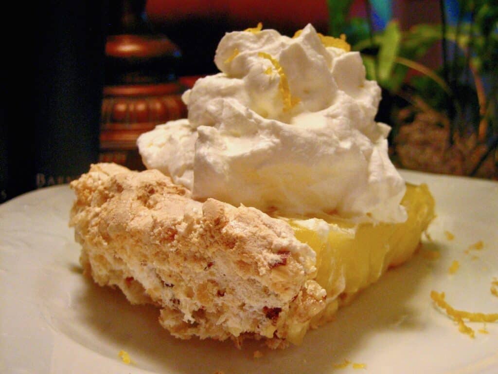 A Slice of Upside Down Lemon Meringue Pie topped with a big dollop of whipped cream and dusted with lemon zest. This photo highlights the crispy crust.