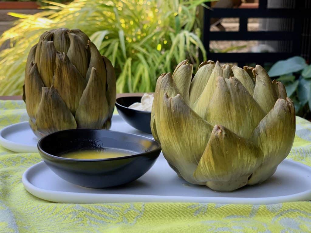 Cooked artichokes served on oval plates with melted butter and Curry Dip.