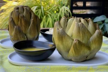 Cooked artichokes served on oval plates with melted butter and Curry Dip.
