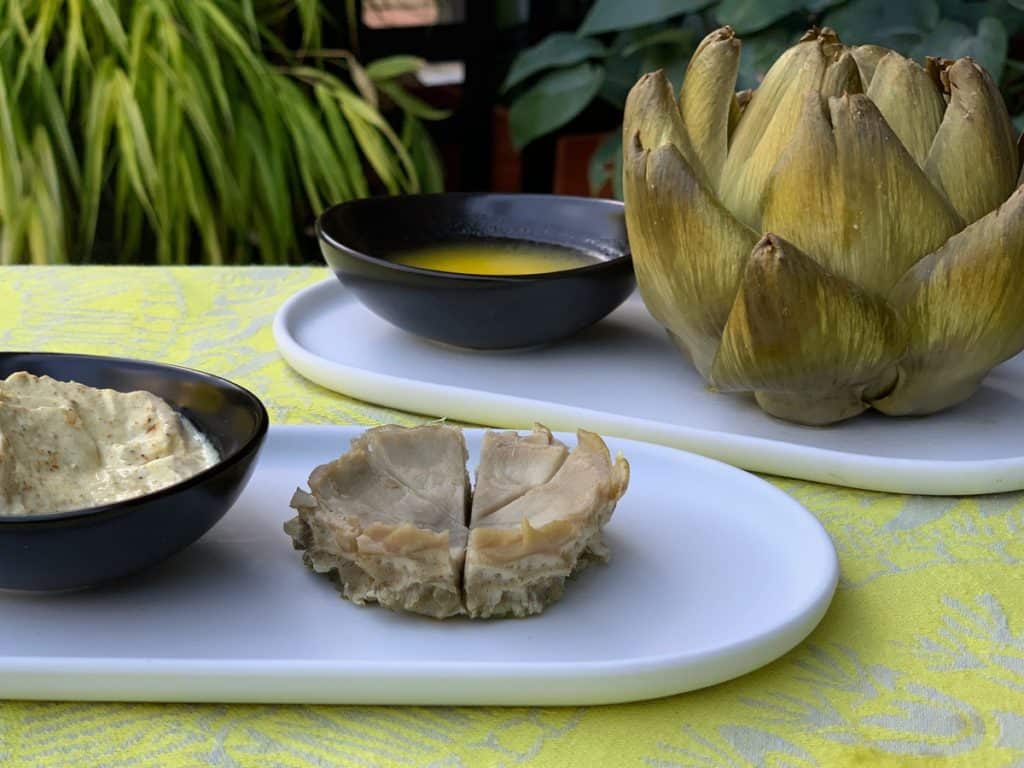 An artichoke heart served with a simple Curry Dip. A whole cooked artichoke is in the background.