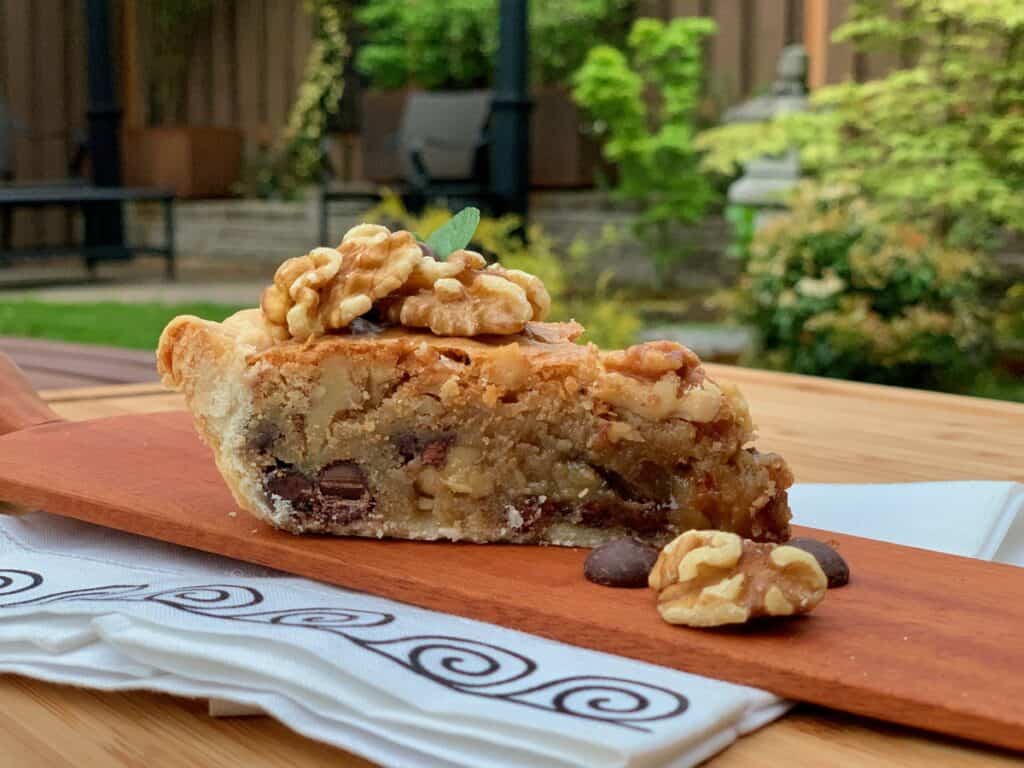 A slice of Aunt Hen's Brownie Pie with walnuts and chocolate chips on a wooden board served in the garden.