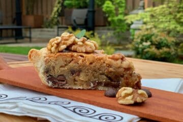 A slice of Aunt Hen's Brownie Pie with walnuts and chocolate chips on a wooden board served in the garden.