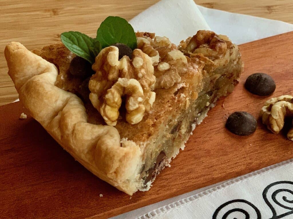 A slice of Aunt Hen's Brownie Pie topped with walnuts and a sprig of mint on a wooden board.