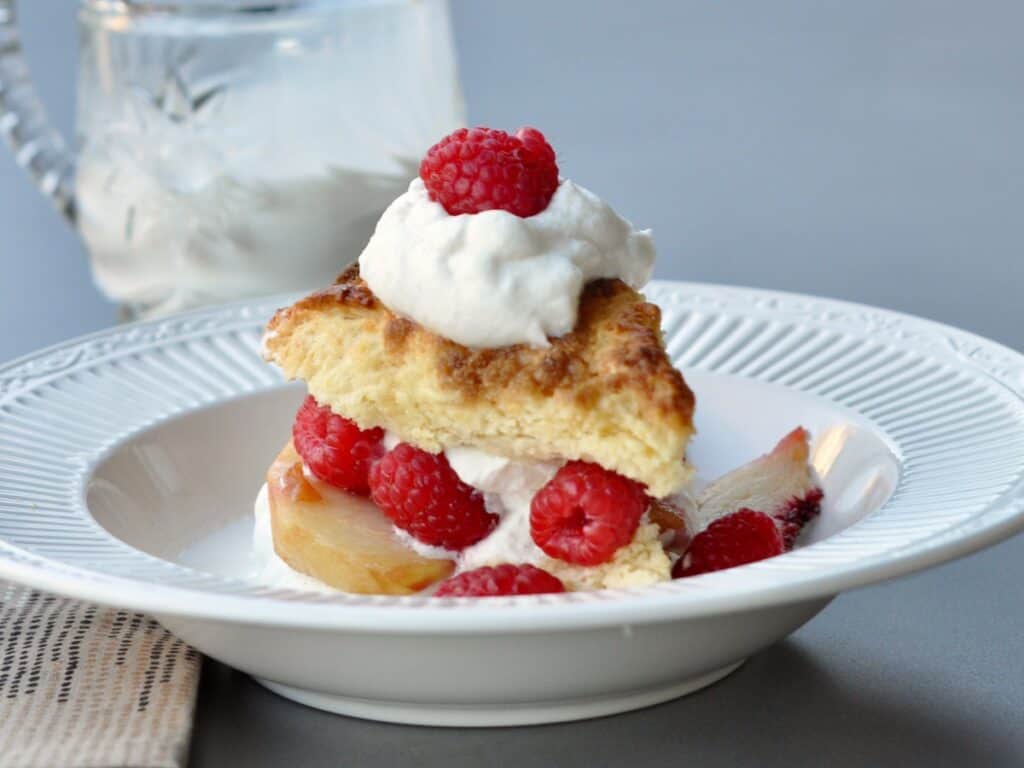 A split Buttermilk Scone layered with raspberries and whipped cream served in a shallow bowl.