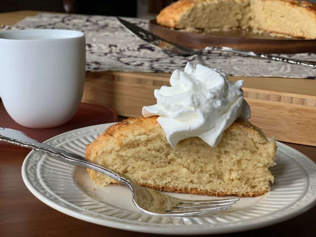 A Buttermilk Scone topped with Whipped Cream and served on a white plate.