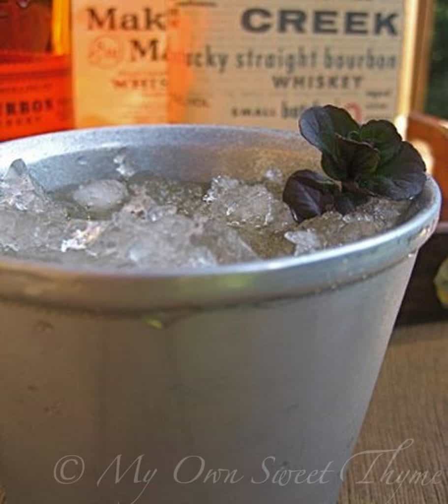 Mint Julep with in a pewter cup with bourbon bottles