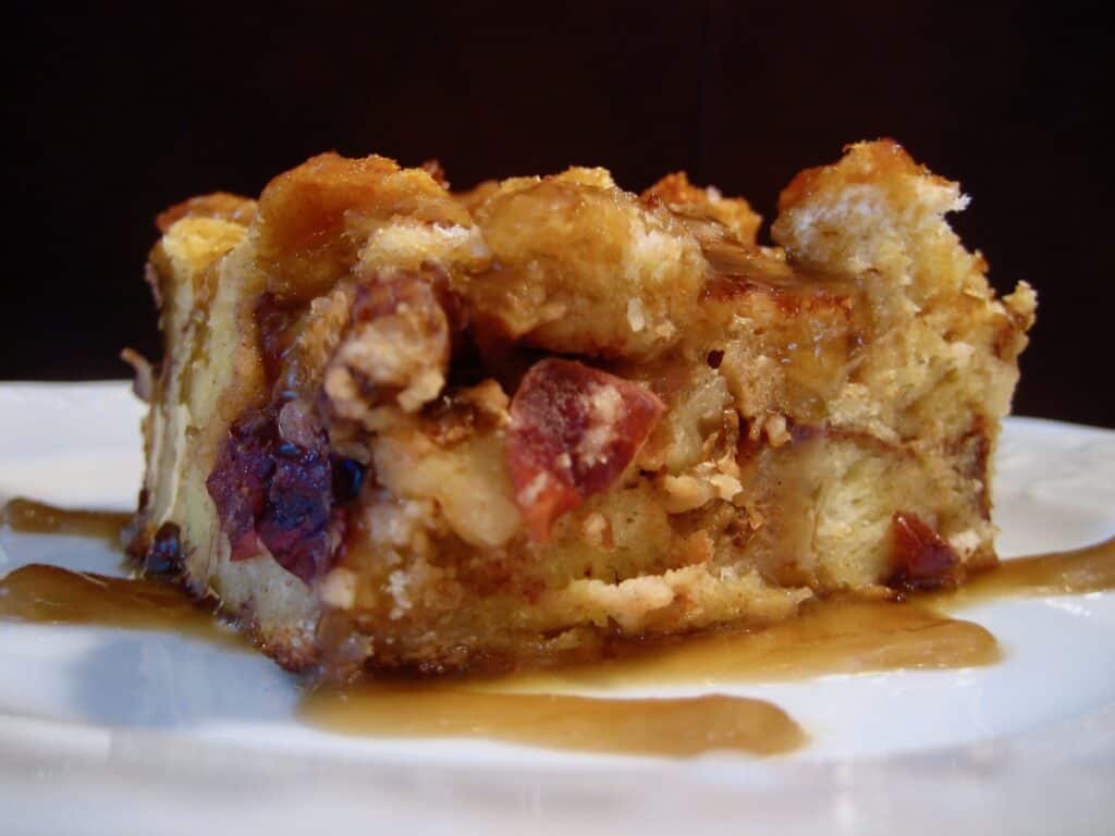 A side view of a square-cut slice of Bread Pudding drizzled with Bourbon Sauce.