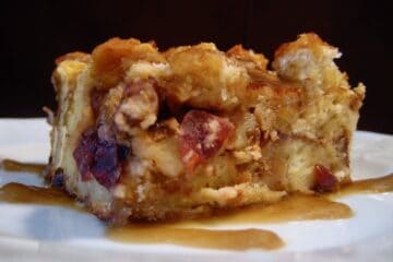 A side view of a square-cut slice of Bread Pudding drizzled with Bourbon Sauce.