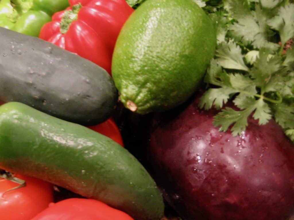 A pile of fresh vegetables, tomato, cucumber, bell pepper, eggplant, lime and parsley, used to make Gazpacho.