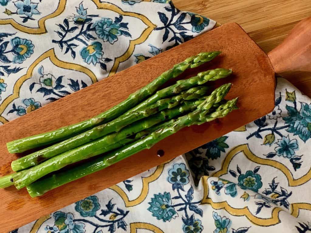 Spears of Roasted Asparagus with Balsamic Vinegar on a wooden serving board atop a French napkin. 