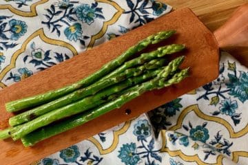 Spears of Roasted Asparagus with Balsamic Vinegar on a wooden serving board atop a French napkin.