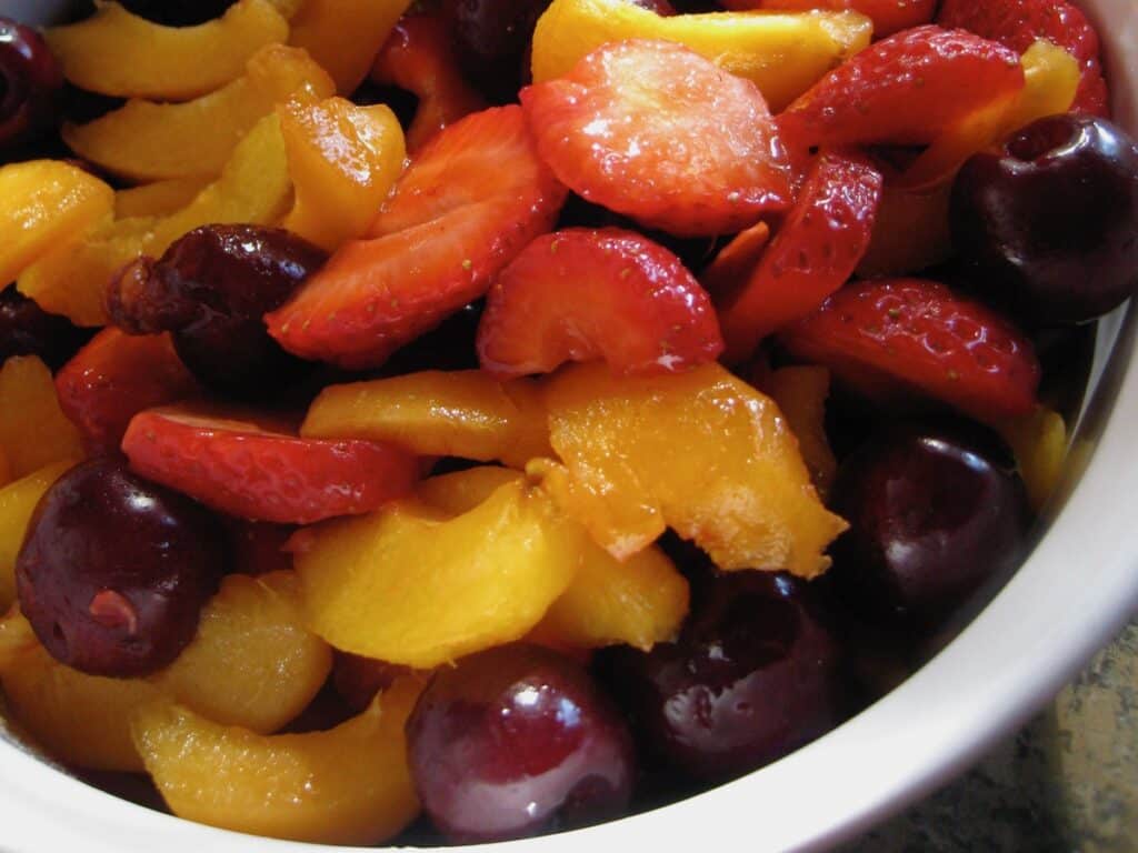 Topped strawberries, pitted cherries, and sliced apricots are combined in a bowl to make Sangria Fruit Salad.