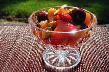 Sangria Fruit Salad with cherries, strawberries and apricots, is served in a footed glass bowl gleaming in the sunshine.
