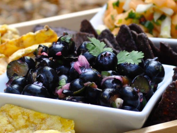 Blueberry Salsa in a square white bowl served with Tortilla chips in a wooden tray