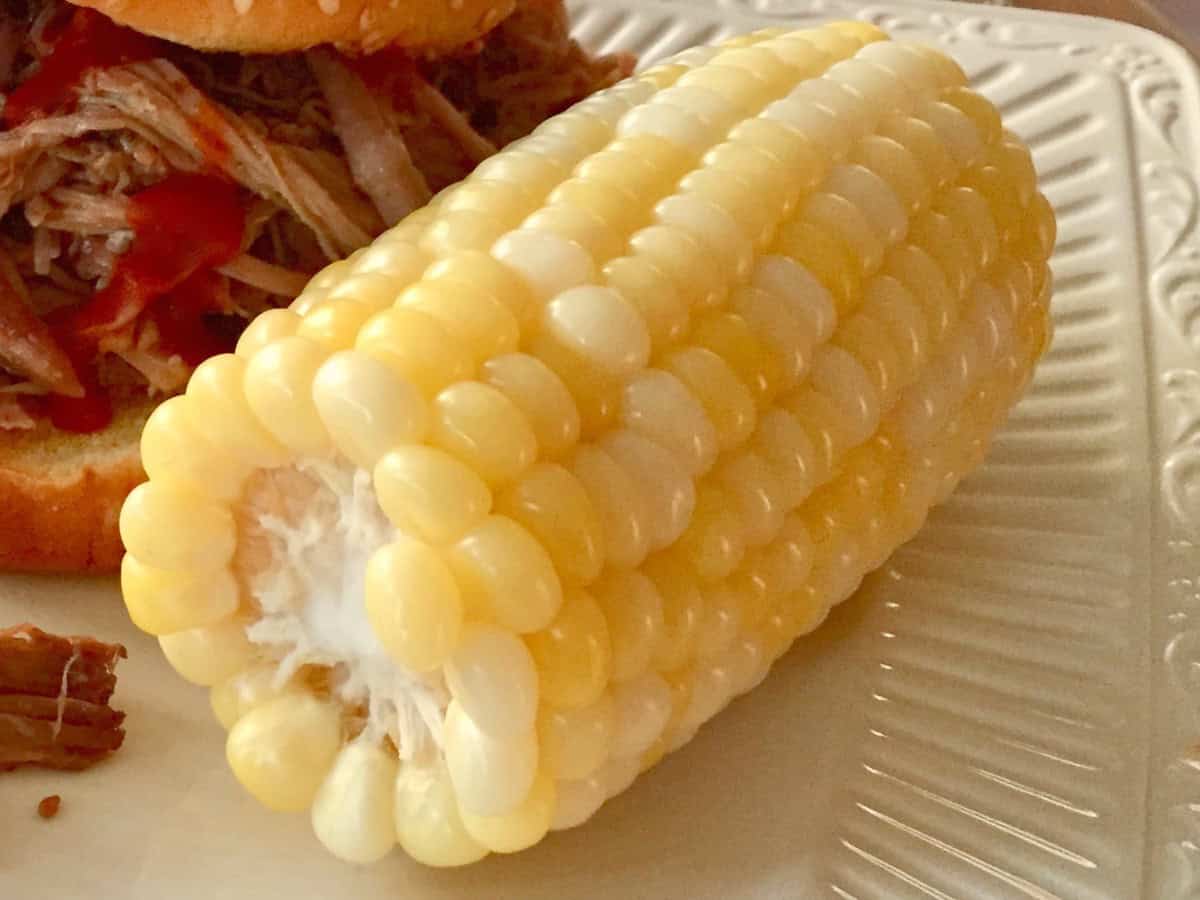 Corn on the Cob served beside a barbecue sandwich.