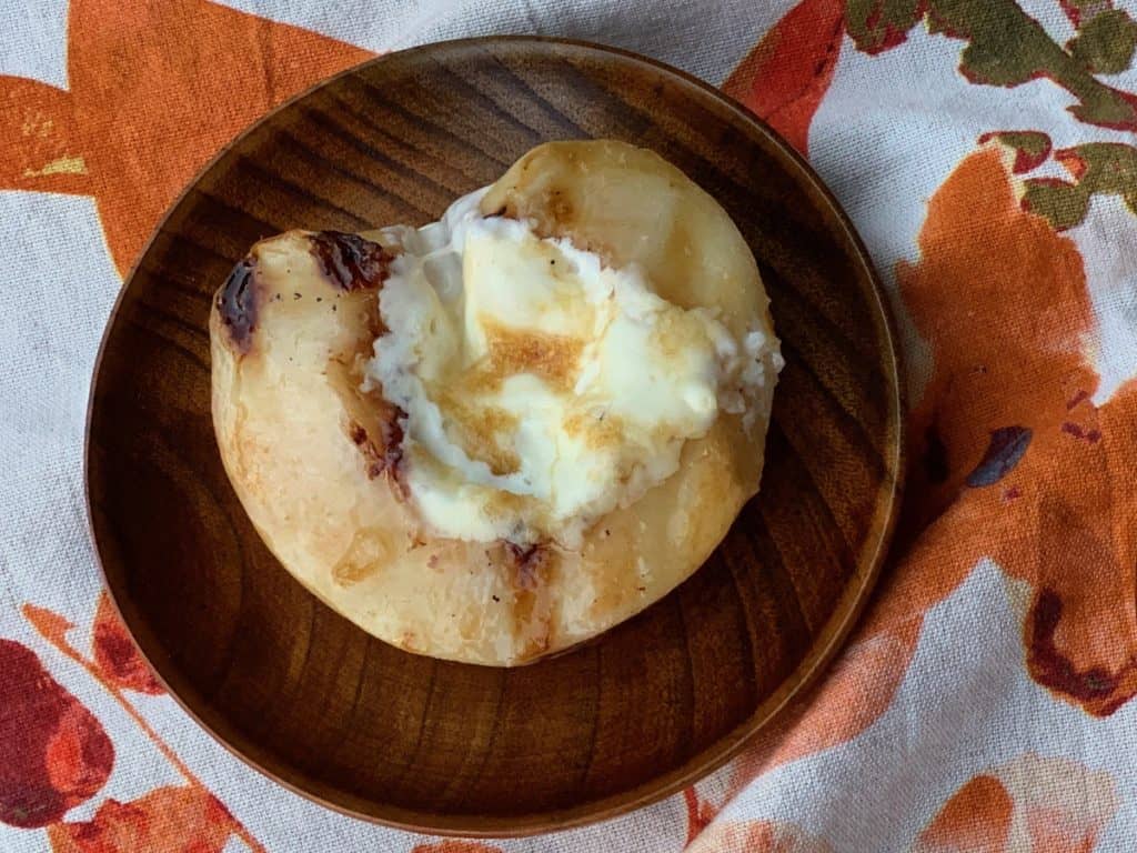 A white peach grilled, filled with mascarpone cheese and drizzled with honey served on a wooden saucer.