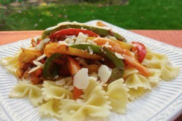 Four Pepper Pasta topped with shredded parmesan on a white plate.