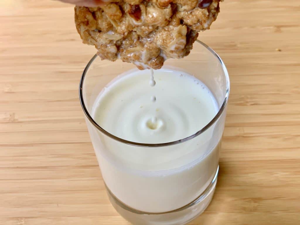 A Soul-Stirring Oatmeal Cookie dipped in a glass of milk and dripping milk back into the glass.