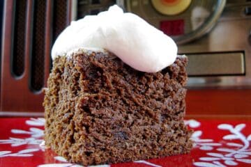 A square of Old-Fashioned Gingerbread topped with Old-Timey Whipped Cream Topping served on a red and white cake.