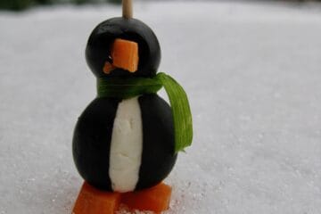 A single Olive Penguin on a toothpick with a scarf made from a strip of chive.