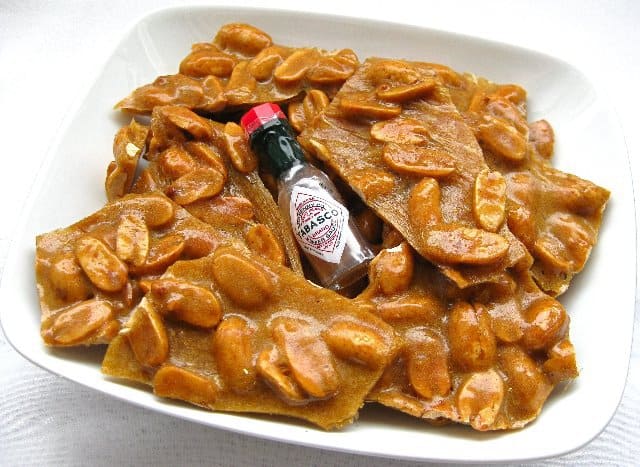 Blistering Peanut Brittle with a tiny bottle of Tabasco in a white bowl