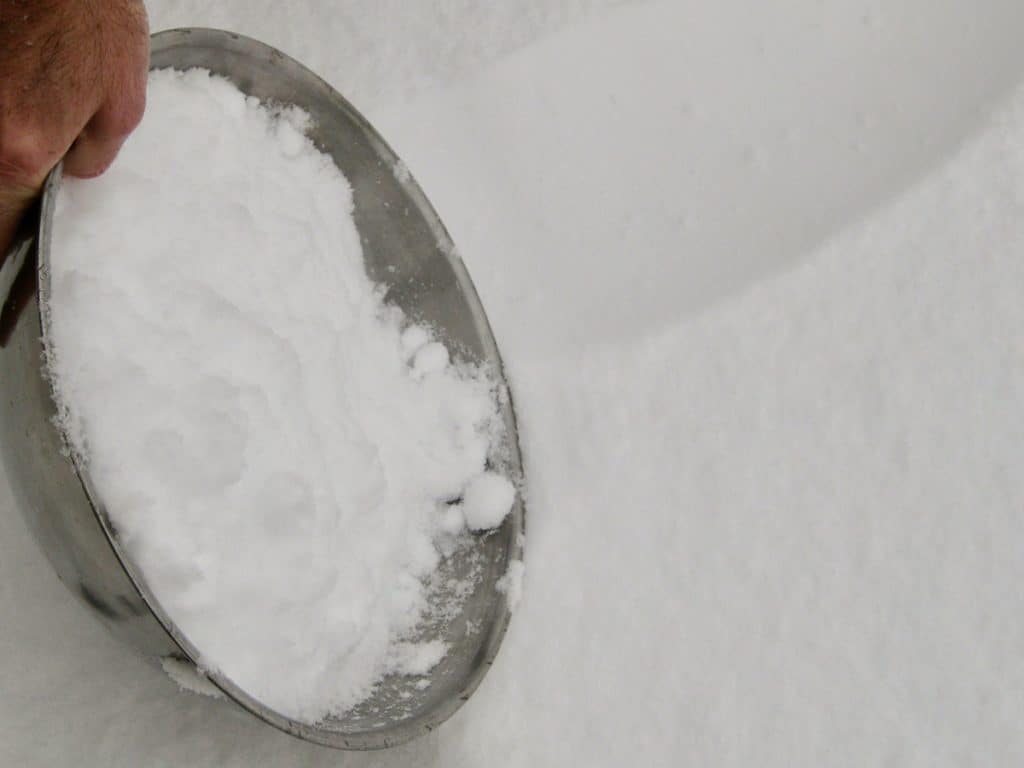 A metal bowl being used to collect clean freshly fallen snow.